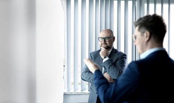 Zwei Geschäftsleute im Gespräch in einem modernen Büro mit weißen Vertikaljalousien im Hintergrund