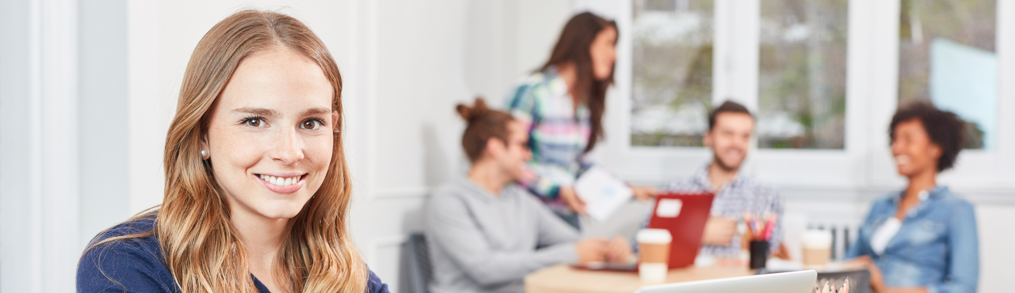 Freundliche Auszubildende in modernem Arbeitsumfeld mit Team im Hintergrund.