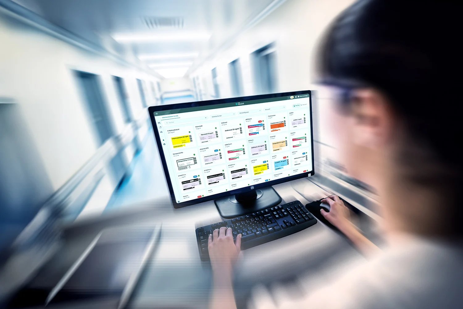 Medizinisches Fachpersonal betrachtet MEDIassist Dashboard auf einem Computerbildschirm im Krankenhausflur.
