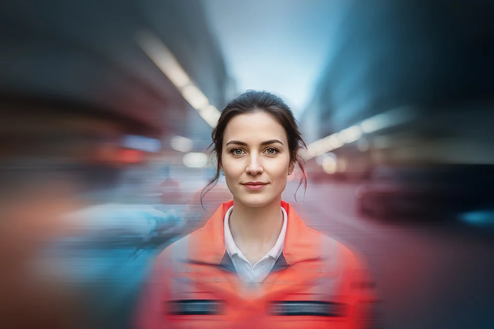Notfallsanitäterin vor unscharfem Rettungswagen in Bewegung.